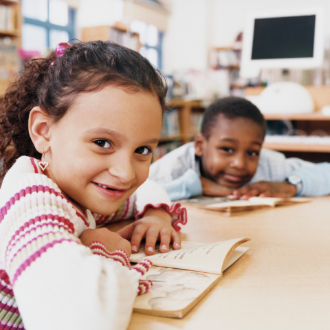 Two young kids smiling with books open in front of them