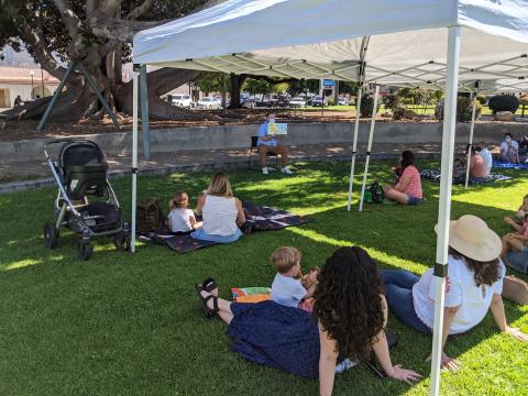 People sitting on Grass, man reading a book.