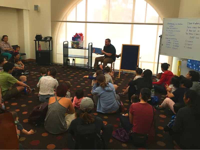 Man reading to group of children and caregivers during storytime