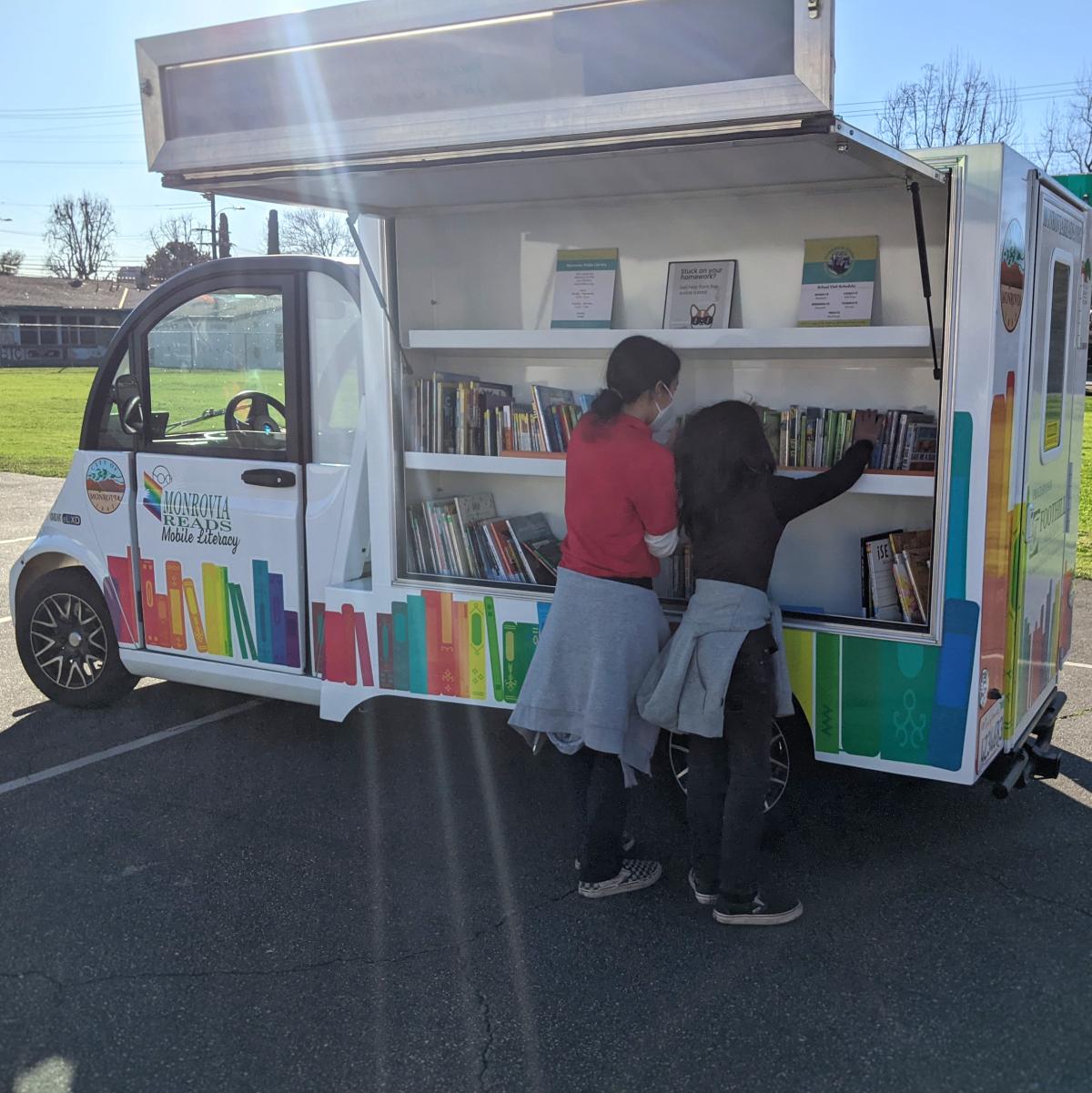 two children reaching for books on the open shelves of the Monrovia Reads Literacy Van